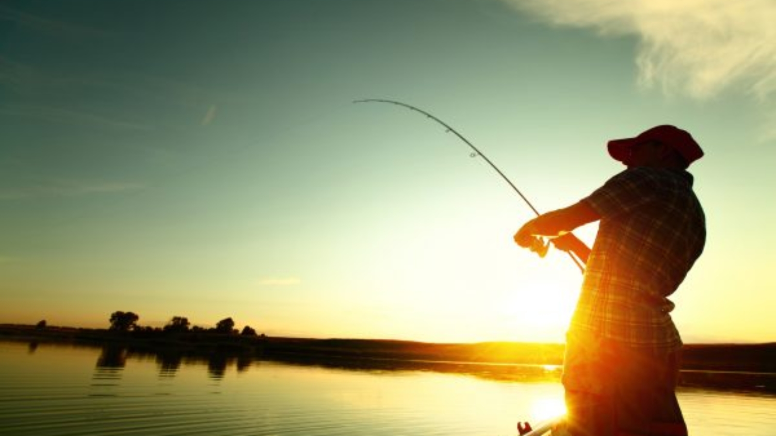 Young man fishing on a lake from the boat at sunset